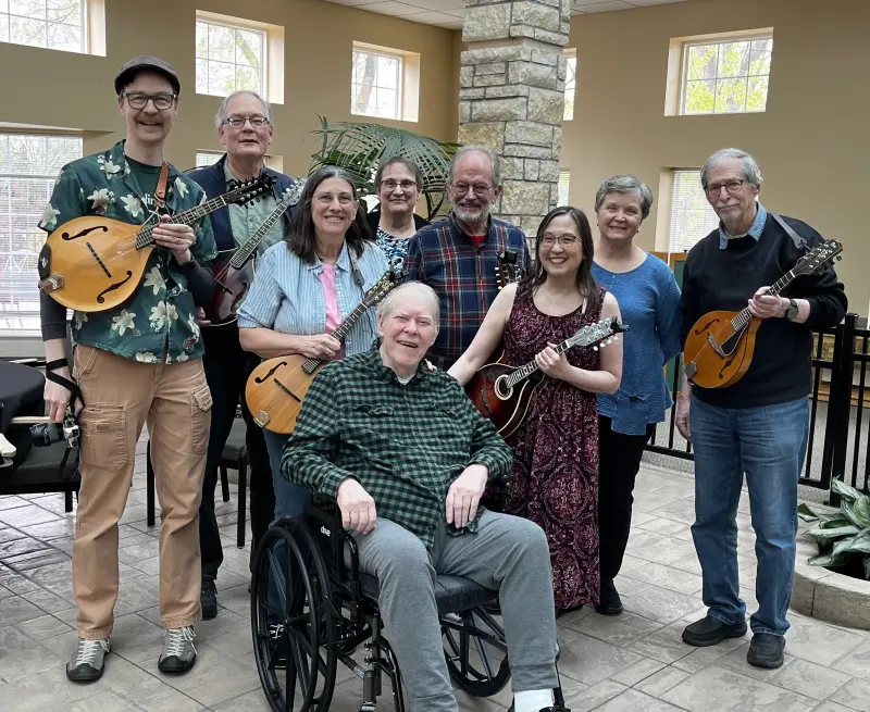 A group of mandolin players stands with a man in a wheelchair